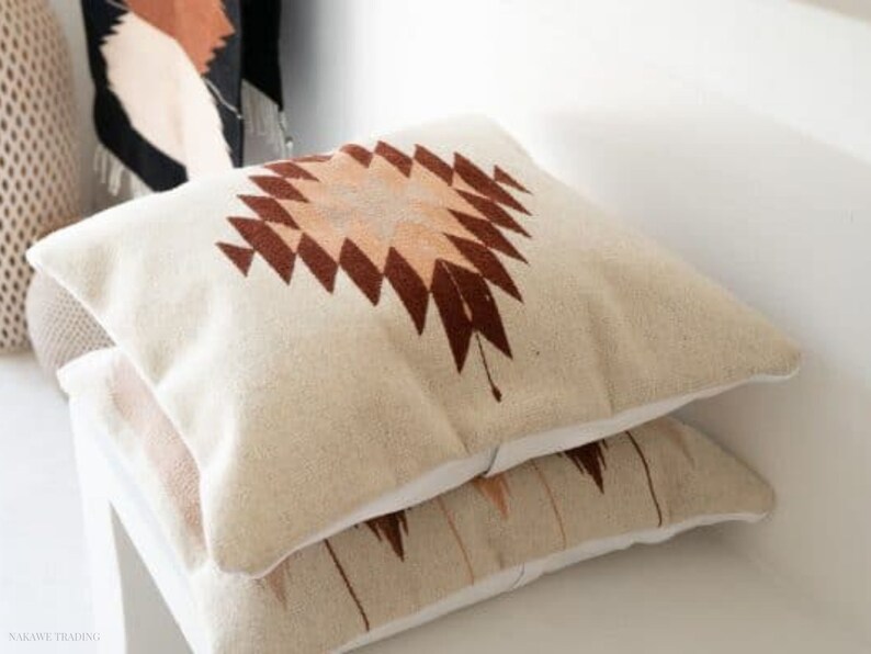 Puede incluir: Dos almohadas de sof&aacute; beige con un patr&oacute;n geom&eacute;trico marr&oacute;n y melocot&oacute;n. Las almohadas est&aacute;n apiladas una encima de la otra.