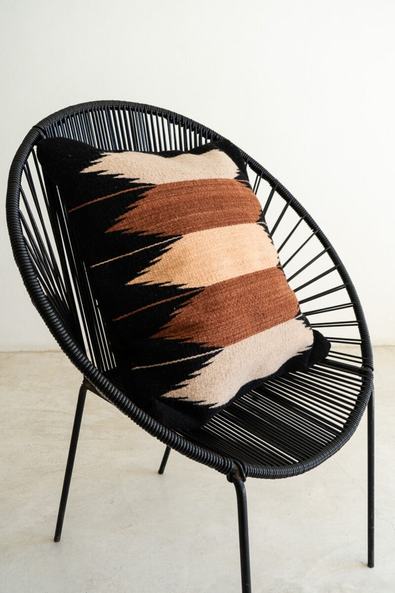 May include: A black woven pillow with a geometric pattern in brown, beige, and black sits on a black metal chair with a circular back.