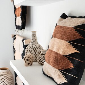 May include: White shelves with a decorative skull, vases, and a pillow with a black, brown, and beige geometric pattern.