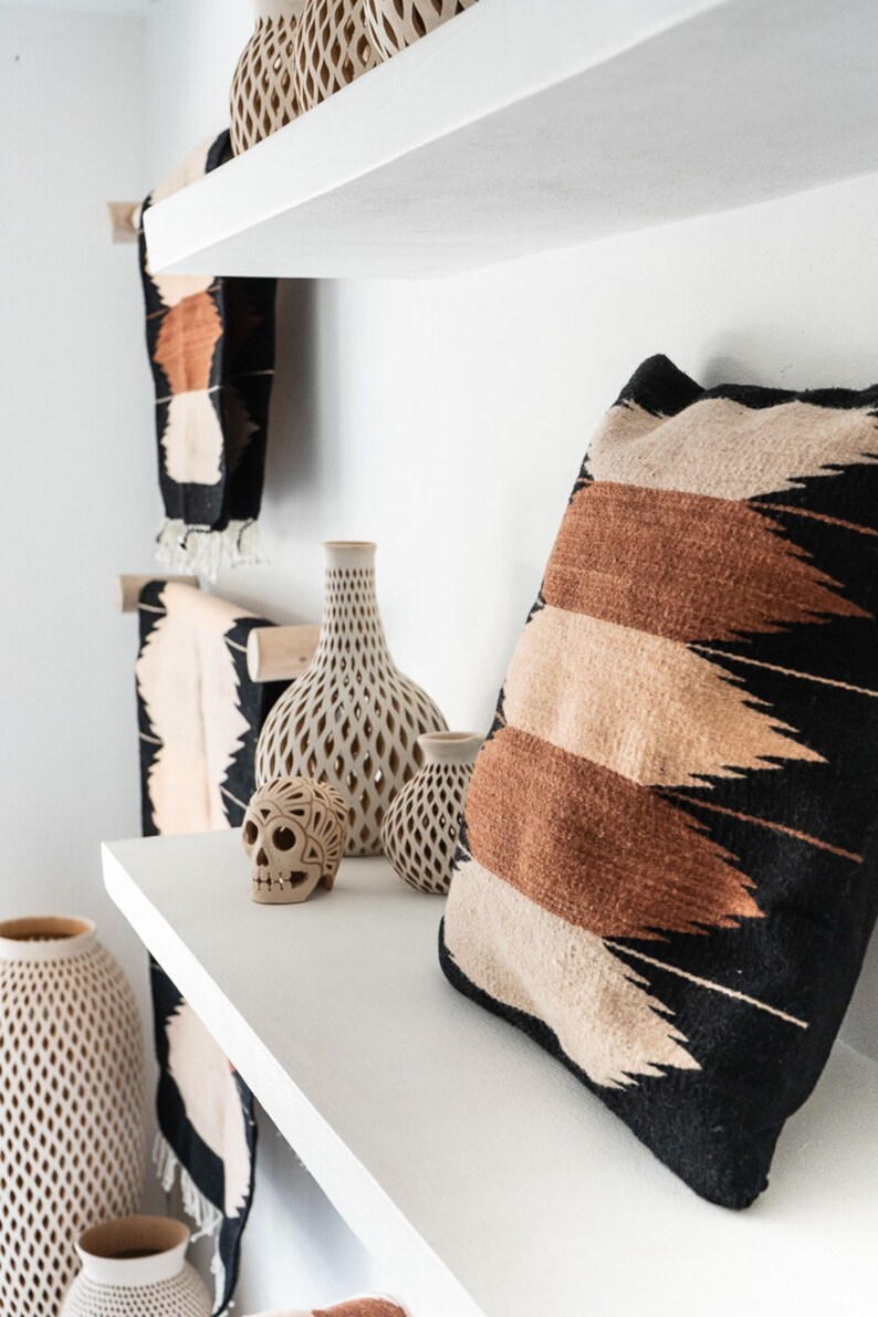 May include: White shelves with a decorative skull, vases, and a pillow with a black, brown, and beige geometric pattern.