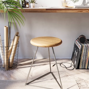 May include: A wooden stool with a round seat and a triangular metal base. The stool is made of light wood and has a natural finish. The metal base is silver in color.