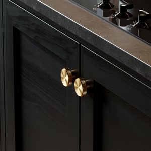 May include: Two gold round cabinet knobs with a textured surface are mounted on a black cabinet door.
