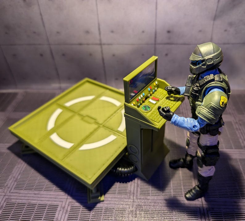 Pu&ograve; includere: Una piattaforma di atterraggio verde e bianca con un pannello di controllo e una action figure verde e blu in piedi accanto ad essa.