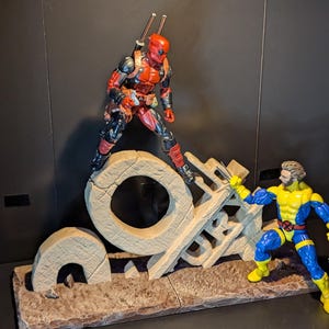 May include: A red and black action figure of Deadpool standing on a stone structure shaped like the number 9. A blue and yellow action figure of Wolverine is standing on the ground, facing Deadpool.