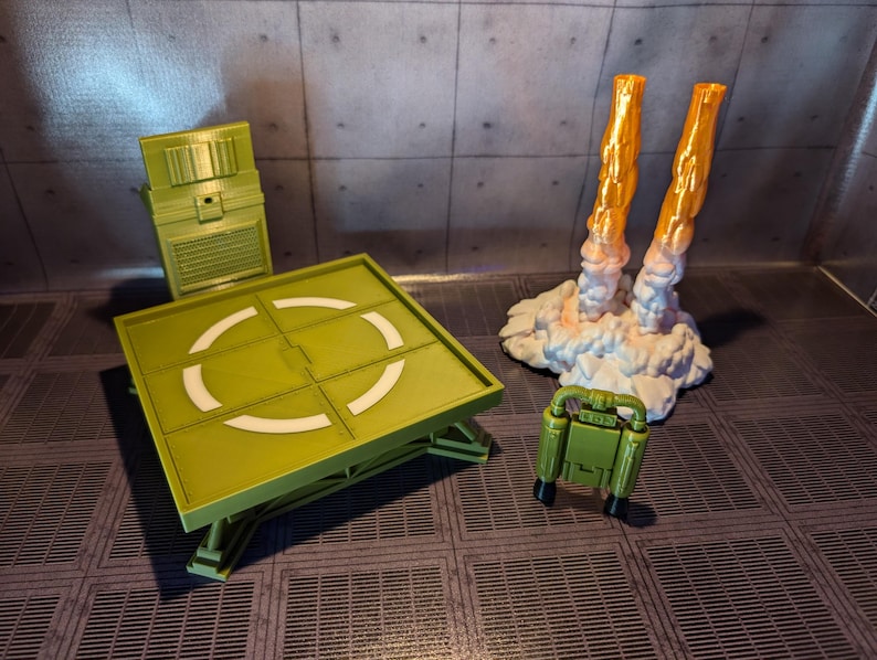 Pu&ograve; includere: Un'area di atterraggio giocattolo verde con un design circolare bianco, un pannello di controllo verde e un jetpack verde con fiamme arancioni.