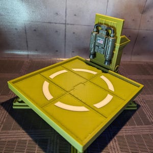 Pu&ograve; includere: Un modello in plastica verde di un'area di atterraggio per elicotteri con una zona di atterraggio bianca e un piccolo modello in plastica verde di un jetpack con una bandiera americana sul lato.