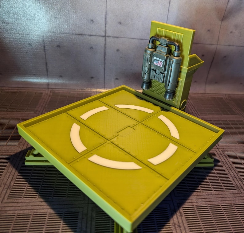 Pu&ograve; includere: Un modello in plastica verde di un'area di atterraggio per elicotteri con una zona di atterraggio bianca e un piccolo modello in plastica verde di un jetpack con una bandiera americana sul lato.