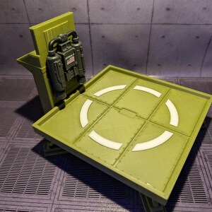 Pu&ograve; includere: Un modello di piattaforma di atterraggio in plastica verde con un design circolare bianco. Un modello di zaino a razzo in plastica verde &egrave; attaccato al lato della piattaforma di atterraggio.