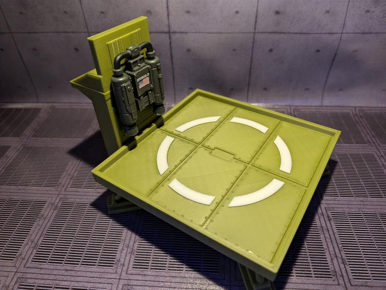 Pu&ograve; includere: Un modello di piattaforma di atterraggio in plastica verde con un design circolare bianco. Un modello di zaino a razzo in plastica verde &egrave; attaccato al lato della piattaforma di atterraggio.