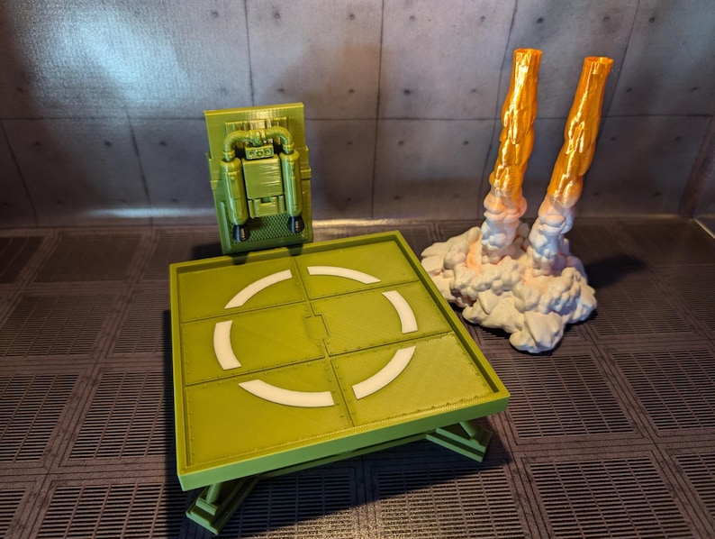 Pu&ograve; includere: Una piattaforma di atterraggio verde con un cerchio bianco al centro. Un jetpack giocattolo verde e nero &egrave; attaccato al muro dietro la piattaforma di atterraggio. Due scarichi di razzi giocattolo arancioni e bianchi sono sul lato destro dell'immagine.