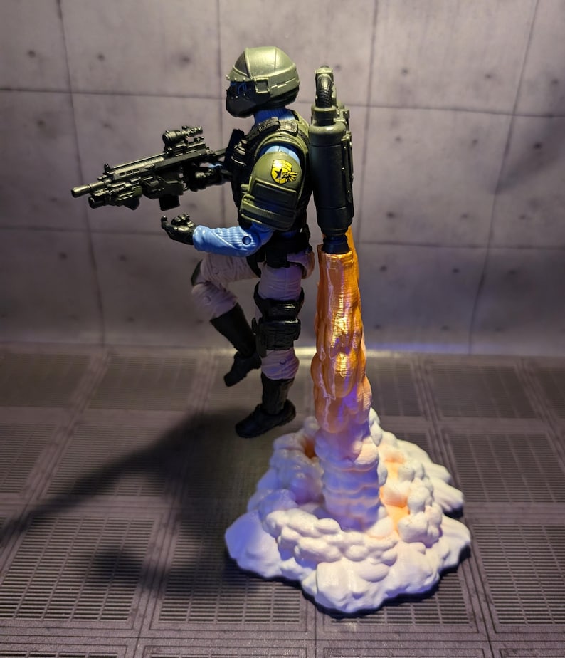 May include: A green and black action figure with a jetpack and a gun, standing on a white cloud with an orange flame coming out of the jetpack.