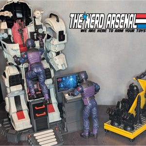 May include: A large white and red toy robot is being worked on by several action figures in blue and purple uniforms. One figure climbs the robot, while another works at a computer. A third figure pushes a yellow cart with black accessories. The text "THE NERD ARSENAL" is visible.