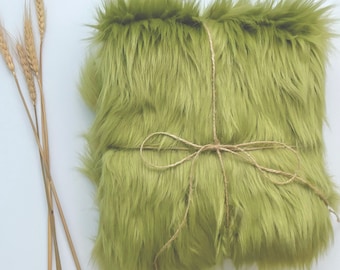 May include: A bundle of soft, green faux fur fabric tied with twine. The fur is long and fluffy, and the fabric is folded in half.