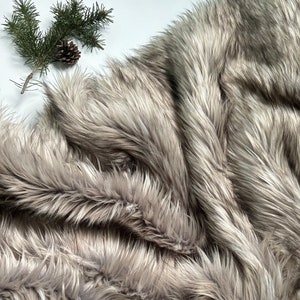 May include: A close-up of a soft, fluffy, gray faux fur fabric. The fur is arranged in a swirling pattern, creating a luxurious and cozy look.