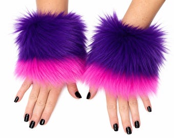 May include: A pair of wrist cuffs made of long-pile faux fur featuring a color-blocked design with a deep purple upper section and a vibrant hot pink lower section. The cuffs are designed to be worn around the wrists, showcasing a thick, fluffy texture.