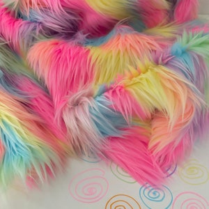 May include: Rainbow colored faux fur fabric with a soft, fluffy texture. The fabric is arranged in a loose pile, showing the different colors.