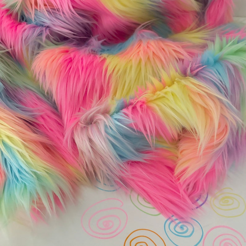 May include: Rainbow colored faux fur fabric with a soft, fluffy texture. The fabric is arranged in a loose pile, showing the different colors.