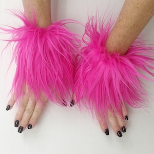 May include: A pair of bright pink fluffy wrist cuffs. The cuffs are made of faux fur and are soft and plush.
