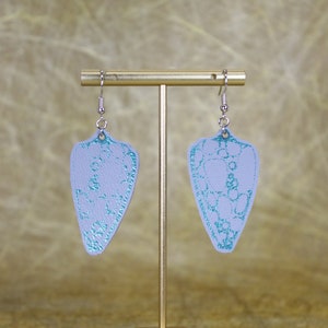 May include: A pair of silver dangle earrings with a light blue, teardrop-shaped pendant. The pendant has a white lace pattern with a teal blue outline.