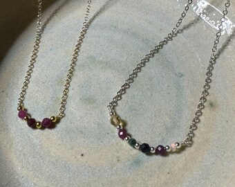 May include: Two silver necklaces with gemstone beads. The top necklace has pink beads and gold accents. The bottom necklace has a variety of colored beads, including pink, green, black, and white.