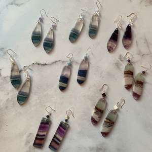 Pode incluir: Um conjunto de 10 pares de brincos com diferentes cores e padr&otilde;es de fluorita. Os brincos s&atilde;o feitos com fechos de ouro e prata e est&atilde;o dispon&iacute;veis em uma variedade de formas, incluindo gota, ret&acirc;ngulo e oval.