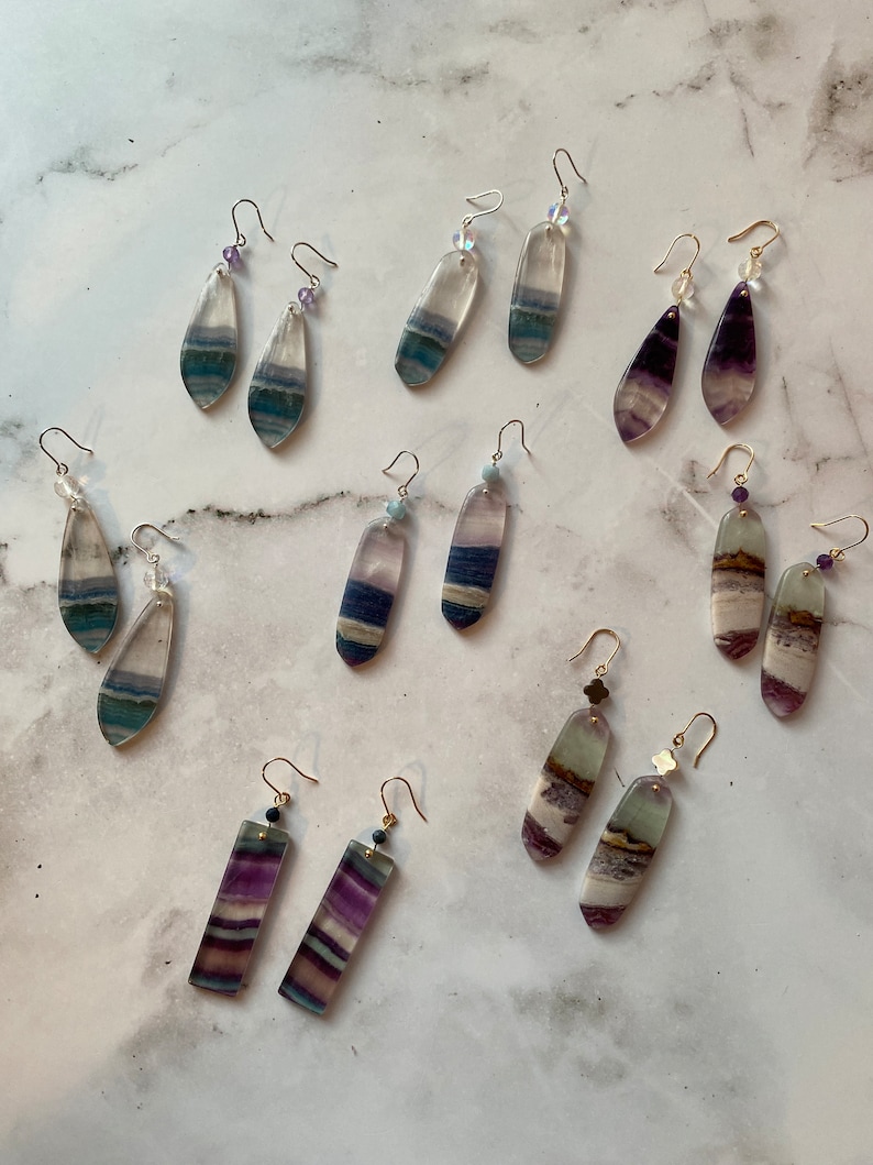 Pode incluir: Um conjunto de 10 pares de brincos com diferentes cores e padr&otilde;es de fluorita. Os brincos s&atilde;o feitos com fechos de ouro e prata e est&atilde;o dispon&iacute;veis em uma variedade de formas, incluindo gota, ret&acirc;ngulo e oval.