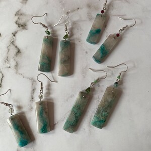 May include: Six pairs of dangle earrings with silver hooks and rectangular green and white stone pendants. Each pendant has a different pattern of green and white.