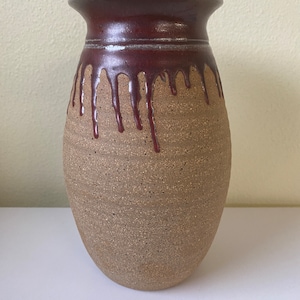 May include: A brown ceramic vase with a dark brown glaze that drips down the sides. The vase has a textured surface and a rounded shape.