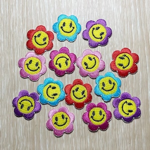 May include: A collection of 14 yellow smiley face iron-on patches with different colored flower designs. The patches are perfect for adding a fun and quirky touch to clothing, bags, or other accessories.