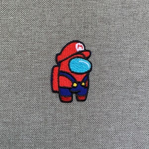 May include: Embroidered patch featuring a red character with a blue visor and a red hat with a white "M" symbol. The character is wearing blue overalls with yellow buttons. The patch is on a gray fabric background.