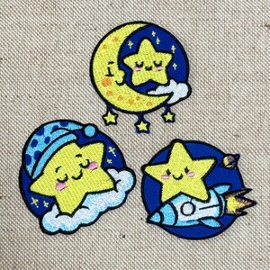 Può includere: Tre toppe ricamate a tema celeste. Una presenta una luna gialla con una stella sorridente, un'altra una stella con un berretto da notte blu e l'ultima una stella su un razzo. Tutte le toppe hanno un bordo blu.