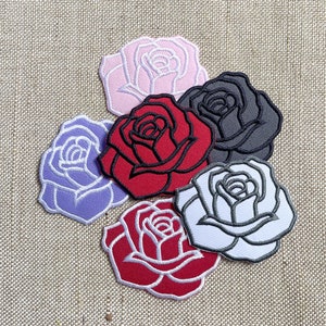 May include: Five embroidered iron-on patches in the shape of roses. The roses are in various colours, including red, pink, white, purple, and grey.