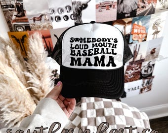 May include: A black and white trucker hat with a white mesh back. The hat has black text that reads "Somebody's Loud Mouth Baseball Mama".