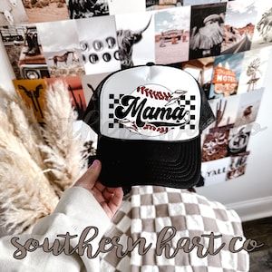 May include: Black and white trucker hat with a white baseball graphic and the word "Mama" in a retro font. The hat has a black mesh back.