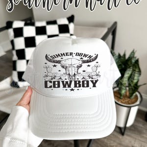May include: White trucker hat with a black and white skull graphic and the text "Summer Down Cowboy".