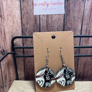 May include: A pair of baseball-themed earrings with a white and black baseball design, a red heart, and the text "HART 50".