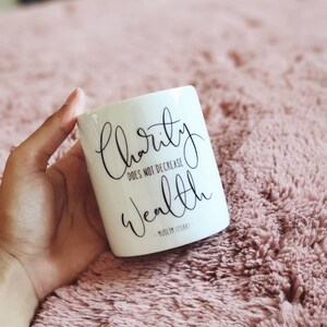 May include: White ceramic mug with black text that reads "charity does not decrease wealth - Muslim 0588 - "