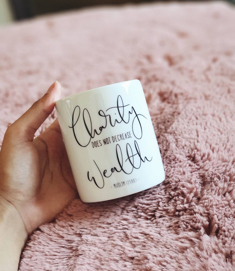 May include: White ceramic mug with black text that reads "charity does not decrease wealth - Muslim 0588 - "