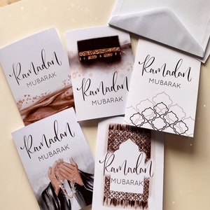 Op de afbeelding: Set van vier wenskaarten met verschillende ontwerpen met islamitische thema's. Elke kaart heeft de tekst "Ramadan Mubarak" in elegante kalligrafie. De ontwerpen omvatten een moskee, een gebedskleed, een hand die gebedskralen vasthoudt en de Kaaba.