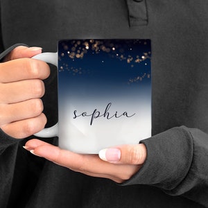 May include: White ceramic mug with a blue and white ombre design. The mug features a scattering of gold glitter and the name "sophia" in black script.