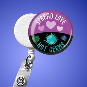 May include: A retractable badge reel with a round, purple and black design. The design features the text "SPREAD LOVE NOT GERMS" with heart and germ illustrations. The reel has a white disc, a metal clip, and a clear plastic strap.