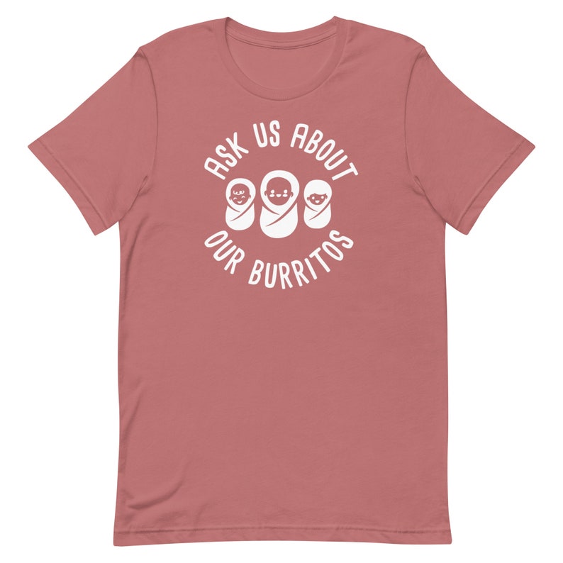 Puede incluir: Una camiseta rosa con un dise&ntilde;o circular blanco que dice "Ask Us About Our Burritos" con tres burritos beb&eacute;s dentro del c&iacute;rculo.