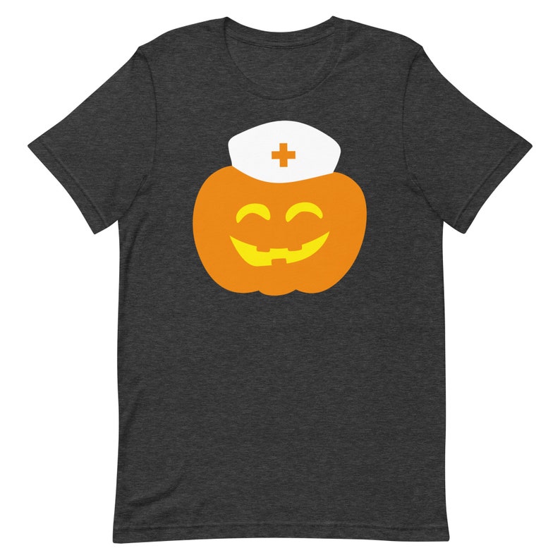 K&ouml;nnte beinhalten: Ein dunkelgraues T-Shirt mit einem Aufdruck einer l&auml;chelnden K&uuml;rbis, die einen wei&szlig;en Krankenschwesterhut mit einem roten Kreuz tr&auml;gt.