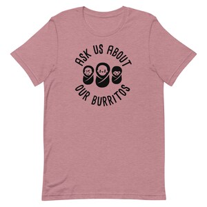 Puede incluir: Una camiseta de color rosa claro jaspeada con un gr&aacute;fico negro que dice "Ask Us About Our Burritos" con tres iconos de beb&eacute;s burritos.