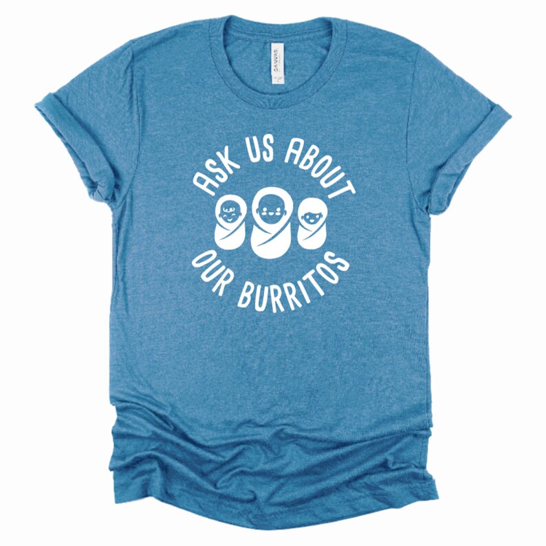 Puede incluir: Una camiseta azul con el texto "Ask Us About Our Burritos" en blanco. Tres caras de beb&eacute;s blancas est&aacute;n dentro del c&iacute;rculo de texto.
