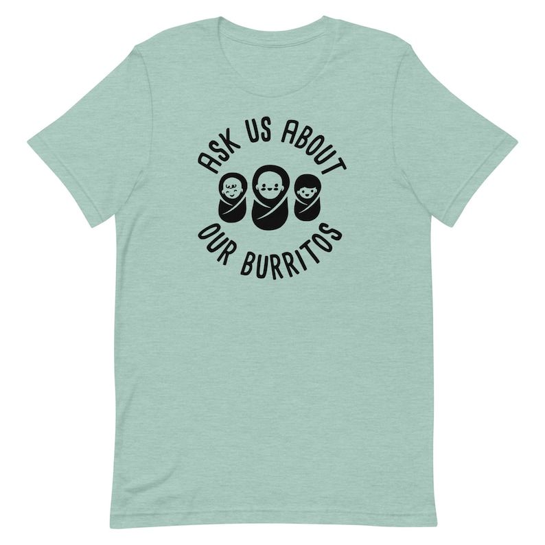 Puede incluir: Una camiseta azul claro con un gr&aacute;fico circular negro que dice "Ask Us About Our Burritos" con tres caras de beb&eacute;s dentro del c&iacute;rculo.