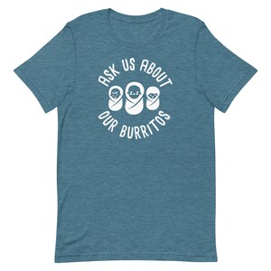 Puede incluir: Una camiseta azul turquesa con un gr&aacute;fico circular blanco que dice "Ask Us About Our Burritos" con tres caras de beb&eacute;s dentro del c&iacute;rculo.