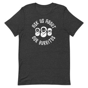 Puede incluir: Una camiseta gris oscuro con un dise&ntilde;o circular blanco que dice "Ask Us About Our Burritos" con tres caras de beb&eacute;s dentro del c&iacute;rculo.