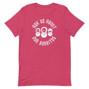 Puede incluir: Una camiseta rosa con un gr&aacute;fico blanco que dice "Ask us about our burritos" con tres caras de beb&eacute;s dentro de un c&iacute;rculo.