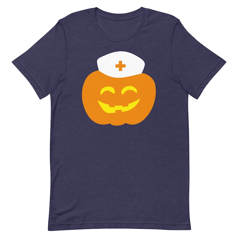 K&ouml;nnte beinhalten: Ein marineblaues T-Shirt mit einem wei&szlig;en K&uuml;rbis, der eine Krankenschwesterm&uuml;tze tr&auml;gt. Der K&uuml;rbis hat ein gelbes, l&auml;chelndes Gesicht.